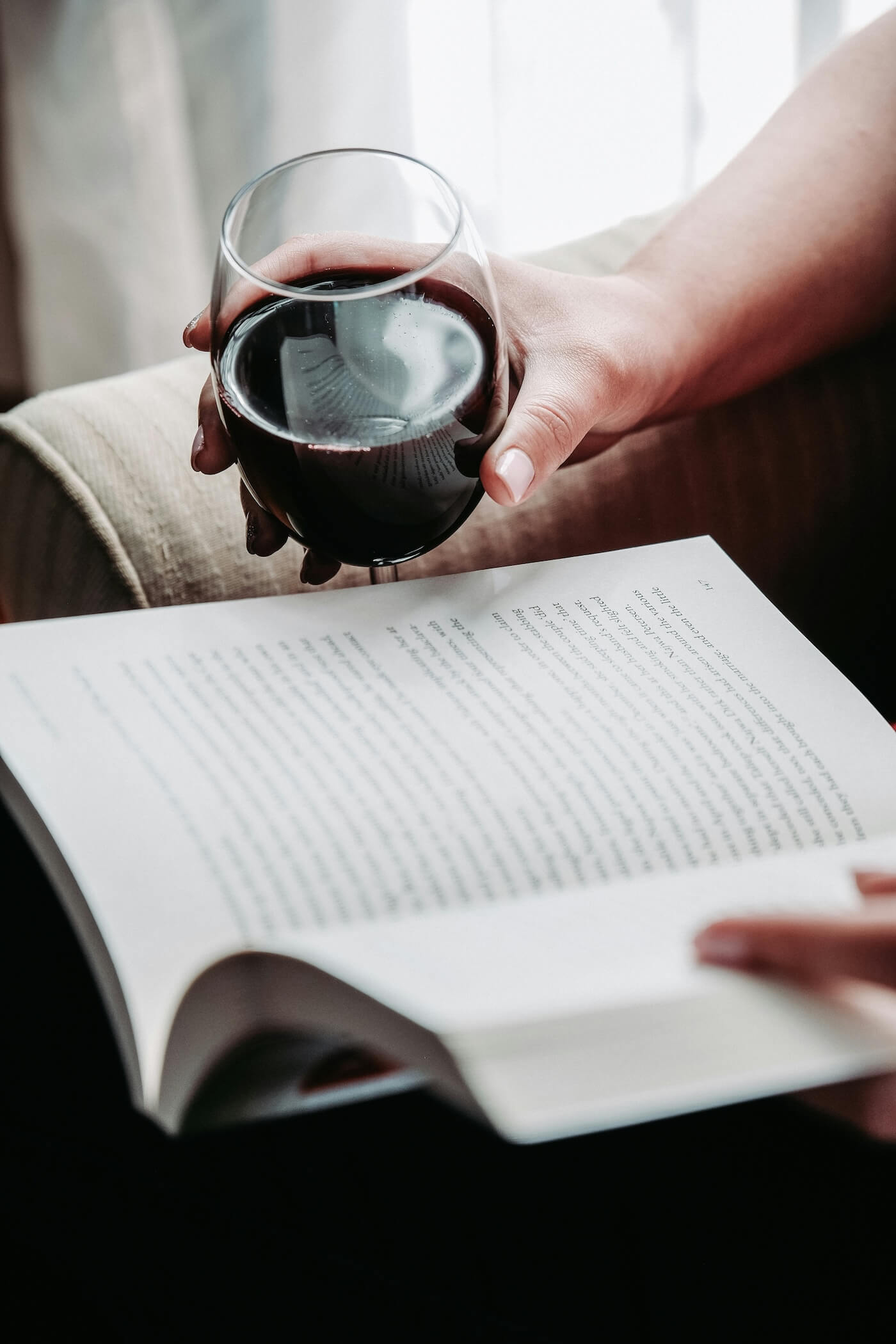 Hand holding a glass of red wine while reading a book